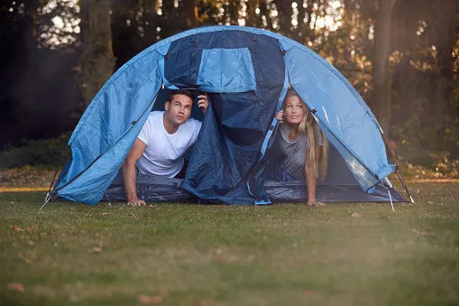 couple worried about weather looking out of tent on camping trip in countryside together