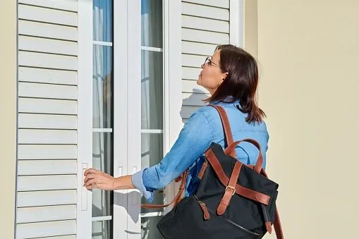 woman closing wooden door with blinds outside the window of a house middle-aged female with a backpack coming or leaving home