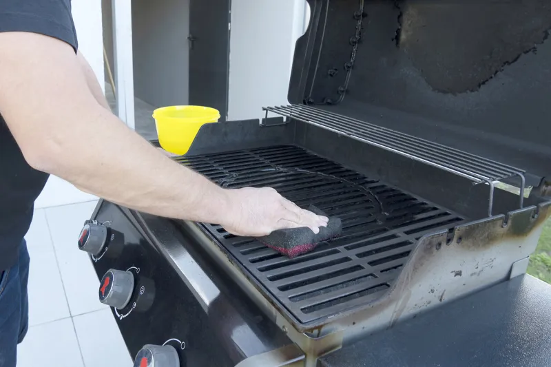 the male hand cleans the black grill with a soft brush grill for frying meat cleaning the outdoor gas grill in the backyard