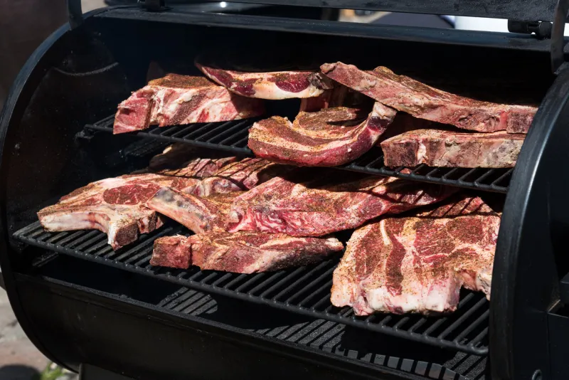 assorted portions of raw seasoned fatty prime ribs ready for the bbq packed out on the shelves of the grill outdoors in a close up view