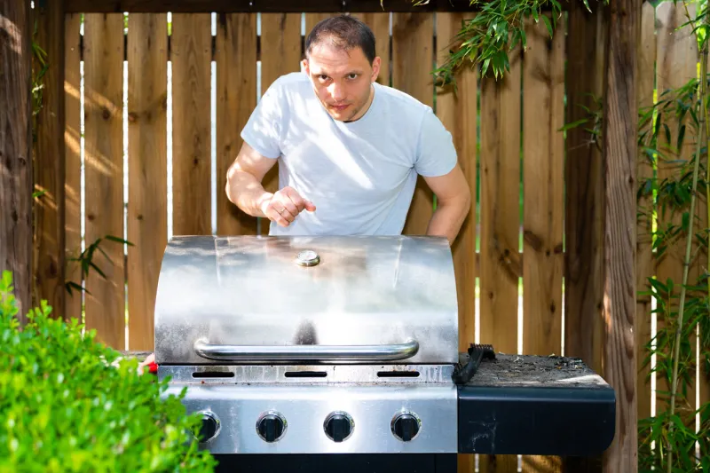 barbeque bbq modern grill in outdoor summer backyard garden during day with man standing opening peeking cover