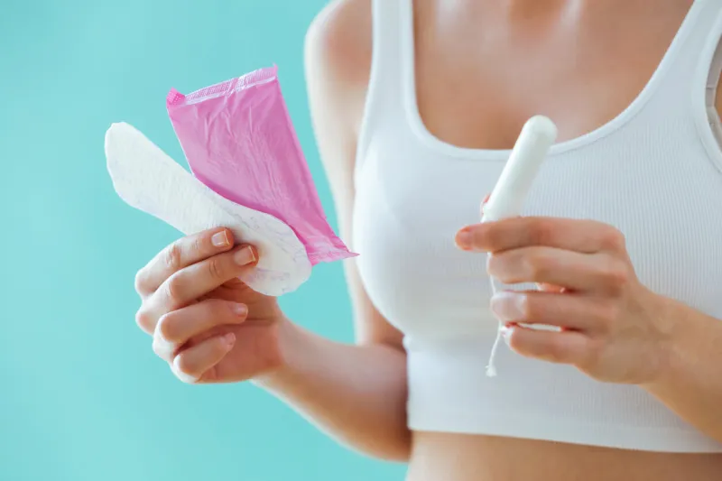 close-up of young woman with a menstrual compress and a tampon on blue background
