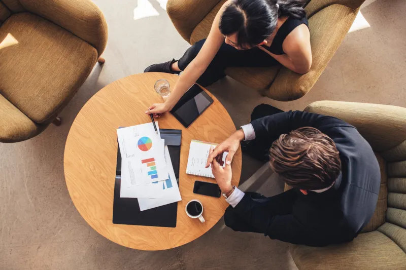 top view of business colleague sitting at table with charts during corporate meeting businessman and businesswoman discussing new project while sitting in office lobby
