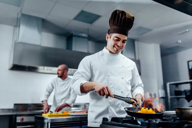 cropped shot of a young man flambeing the fruits in a professional kitchen