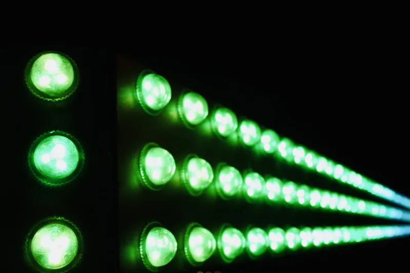close up of lines of green round fun fair led lights at night on black background