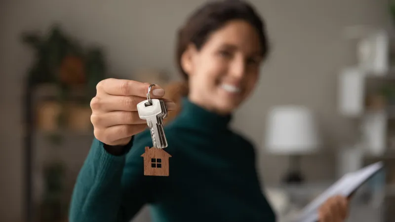 close up focus on keys, smiling woman real estate agent selling apartment, offering to client, showing at camera, holding documents, contract, making purchasing deal, real estate agent, mortgage or rent