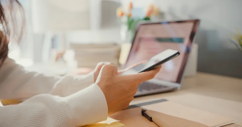 close-up young asia lady freelance focus mobile phone chat with colleagues work finance graph account chart market plan in laptop at home girl student learn online at house, work from home concept