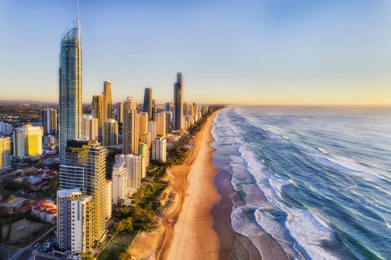 waterfront behind sandy beach of surfers paradise greeting rising sun over pacific ocean aerial view along gold coast and line of high-rise towers