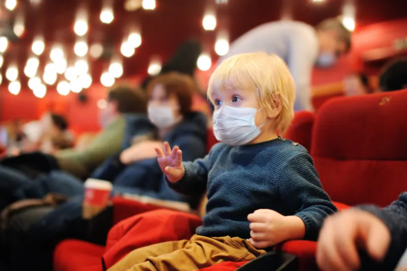 cute toddler boy wearing face mask watching cartoon movie in the cinema lifting virus lockdown social distancing restrictions remain leisure or entertainment for family with kids after quarantine