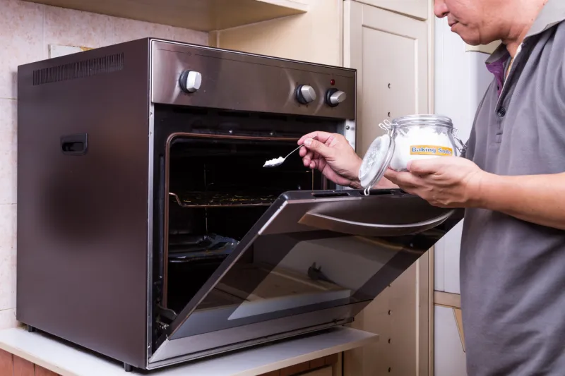 person sprinkling baking soda into an oily oven as cleansing agent to clean