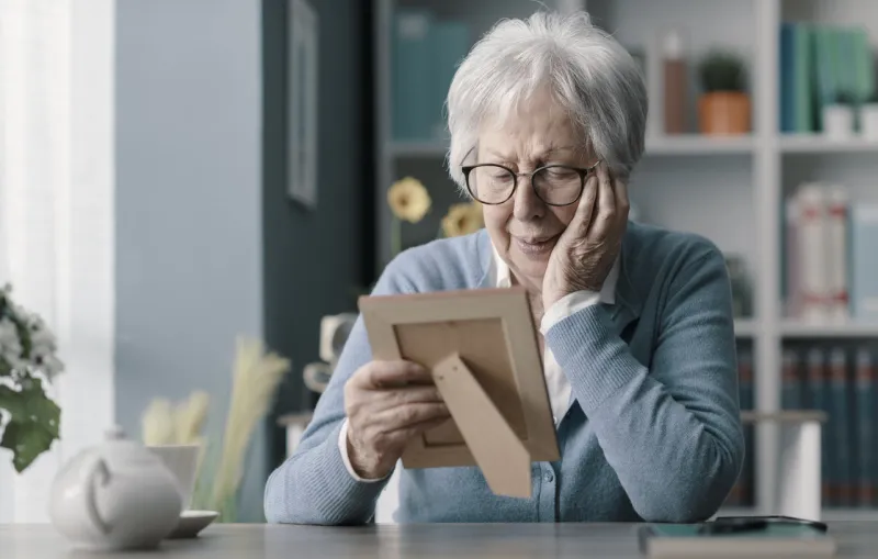 sad senior woman mourning the loss of her husband, she is holding a picture and crying