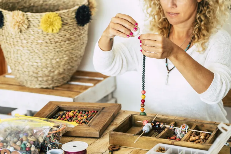 woman at home make handmade jewellery box with beads on old wooden table view with woman hands - tutorial to learn how to make bracelets and jewellery online and alternative home job