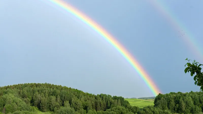 double rainbow on a gray sky after rain a rare atmospheric phenomenon after a storm beautiful hilly landscape with a real rainbow after rain on a summer day