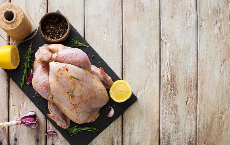 raw whole chicken with lemon, rosemary and garlic on natural wooden table flat lay copy space