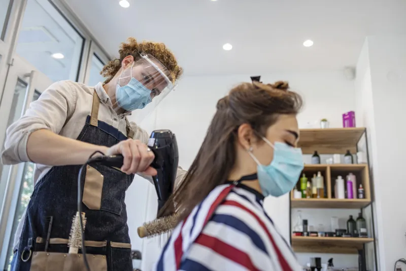 woman have hair cutting at hair stylist during pandemic isolation, they both wear protective equipment hairdresser and customer in a salon with medical masks during virus pandemic working with safety mask