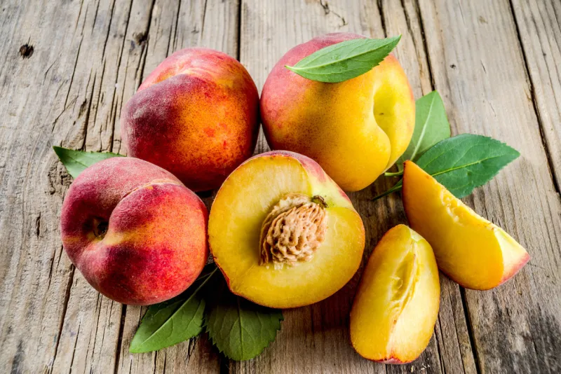 fresh organic peaches, whole and sliced, with leaves, on rustic wooden background