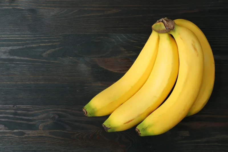 bunch of bananas isolated on dark brown wooden table with free space for text and design