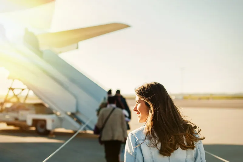 woman tourist passenger getting in to airplane at airport, walking from the terminal to the plane