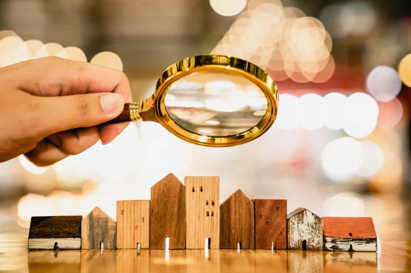 hand holding magnifying glass and looking at house model, house selection, real estate concept