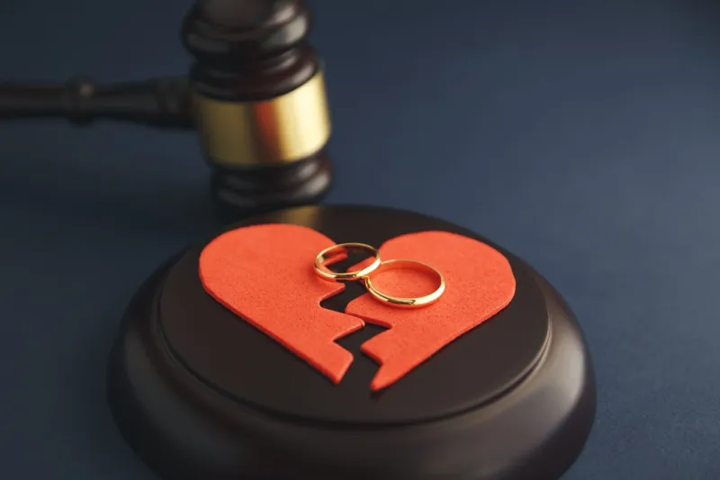 wedding rings on the figure of a broken heart from a tree, hammer of a judge on a wooden background divorce proceedings