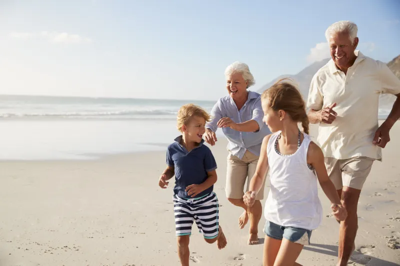 grandparents running along beach with grandchildren on summer vacation