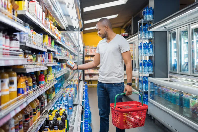 african man shopping in beverage section at supermarket black man doing shopping at market while buying cold drink handsome guy holding shopping basket reading nutritional values of product