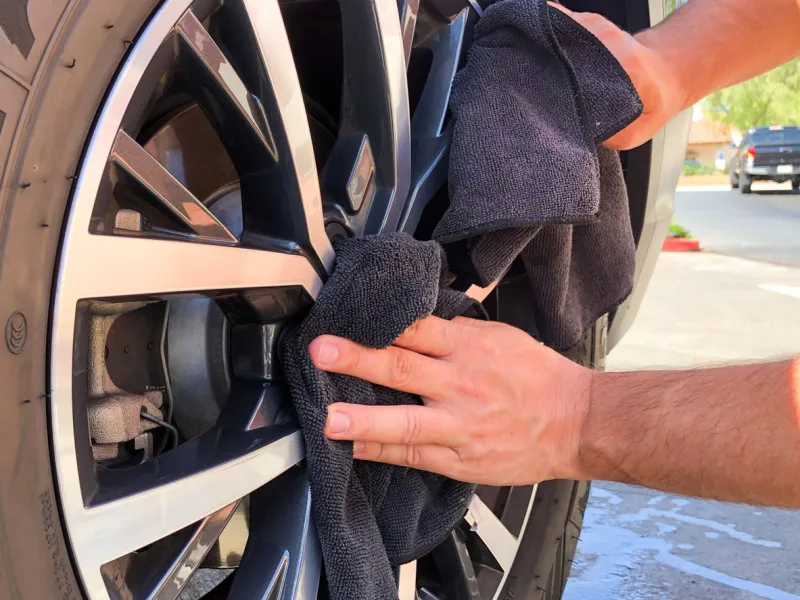 man's hand cleaning wheel and tire with black microfiber cloth hand wipe down shiny rims surface of car car detailing and car wash concept