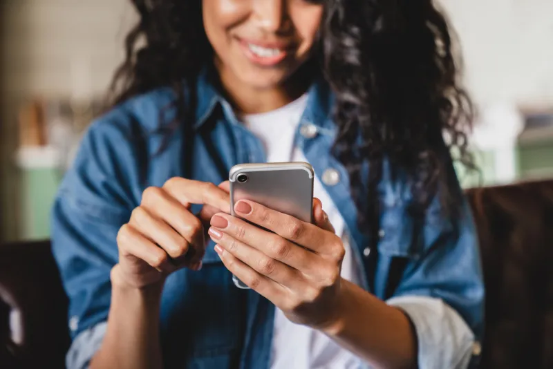 cropped shot of an african-american young woman using smart phone at home smiling african american woman using smartphone at home, messaging or browsing social networks while relaxing on couch