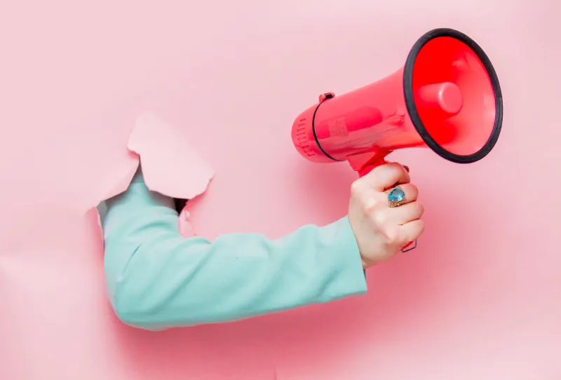 female hand in classic blue jacket with megaphone looks out from pink background