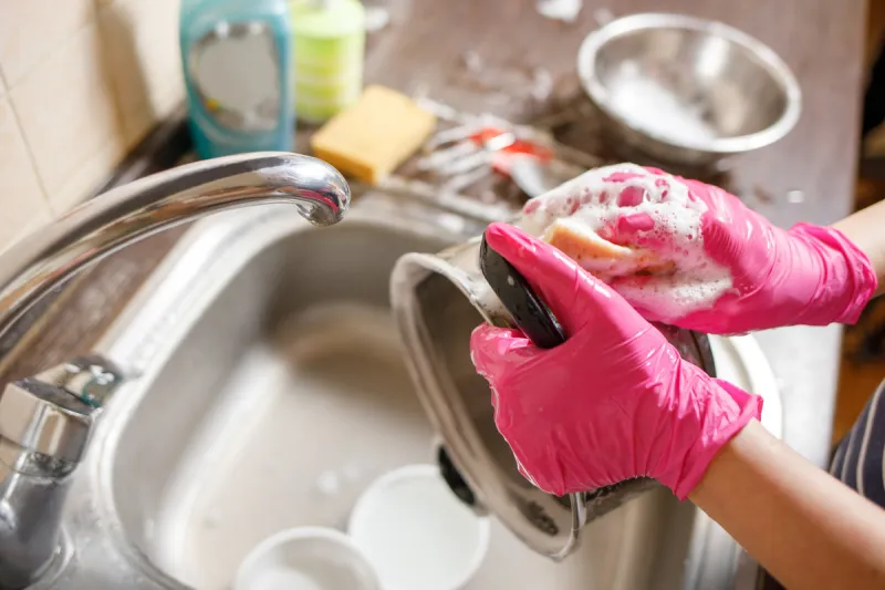woman in rubber gloves washing up dishes and pot stay home clean house