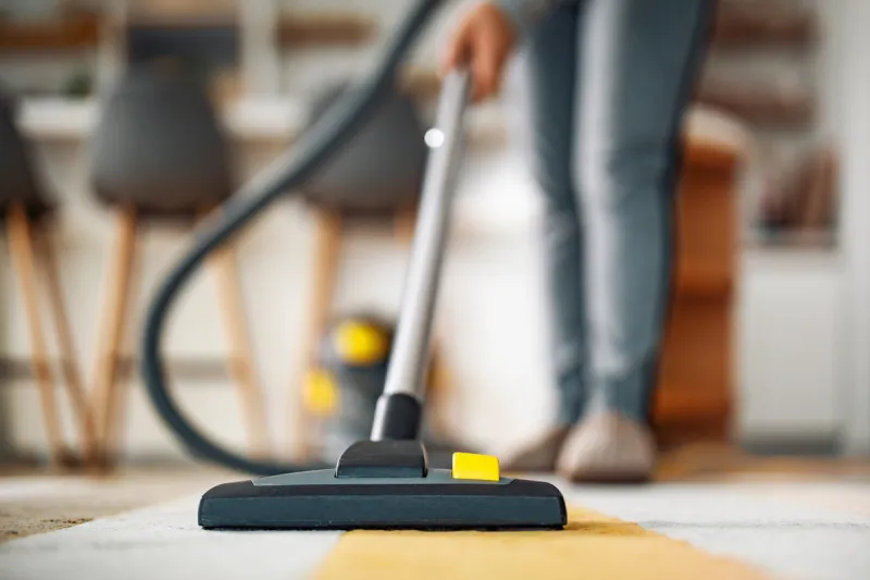 woman using a vacuum cleaner while cleaning carpet in the house