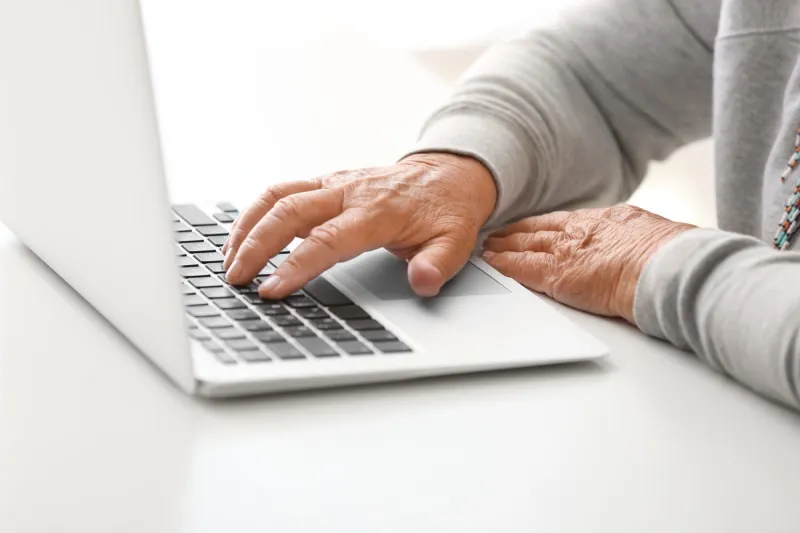 elderly woman with modern laptop sitting at table, closeup