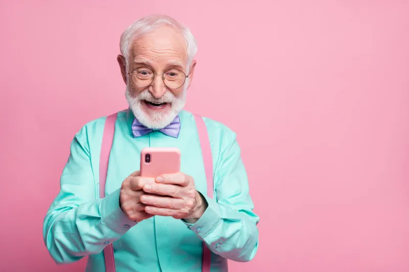 portrait of surprised crazy shocked old man use smartphone read, social media news enjoy comments wear teal outfit purple violet bow tie isolated pastel pink color background