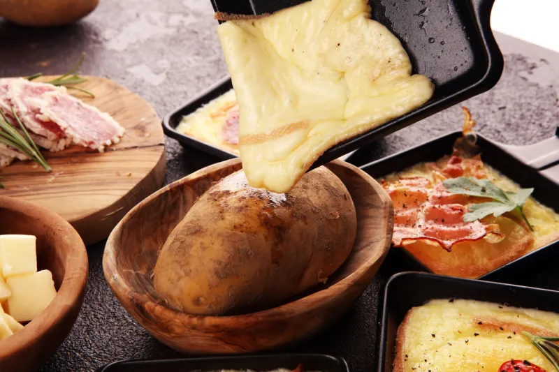 delicious traditional swiss melted raclette cheese on diced boiled or baked potato served in individual skillets with salami and potatoes