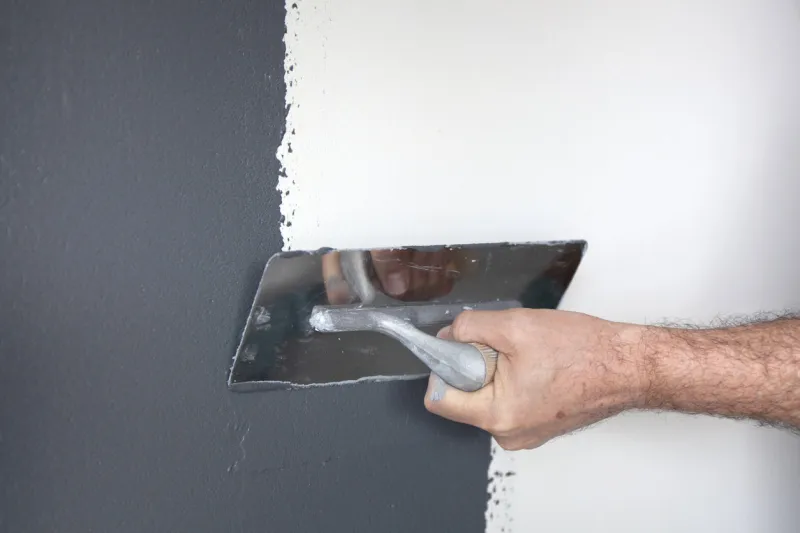 hand with a trowel plastering a wall with decorative plaster