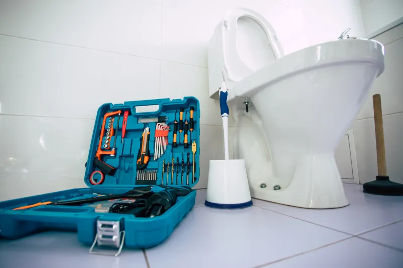 close up photo of ceramic bowl toilet in domestic bathroom with a box of tools