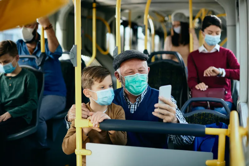 happy grandfather and grandson wearing protective face masks and taking selfie while commuting by bus