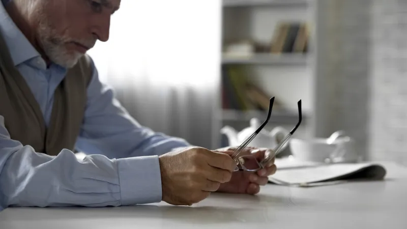 lonely elderly man sitting at table taken off his glasses, eyesight problems