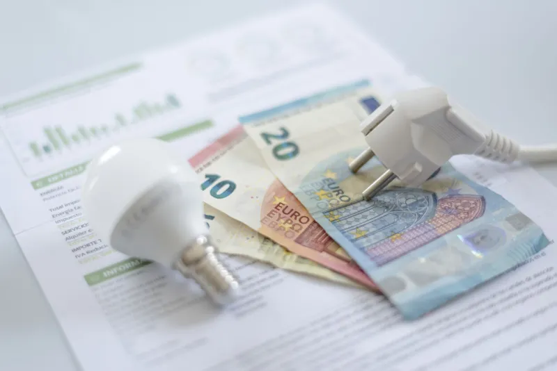 a white electric cap, a light bulb and euro banknotes on an electric bill increase in the cost of electricity for residential customers and business users payment of electricity bills increasing the concept of electricity prices