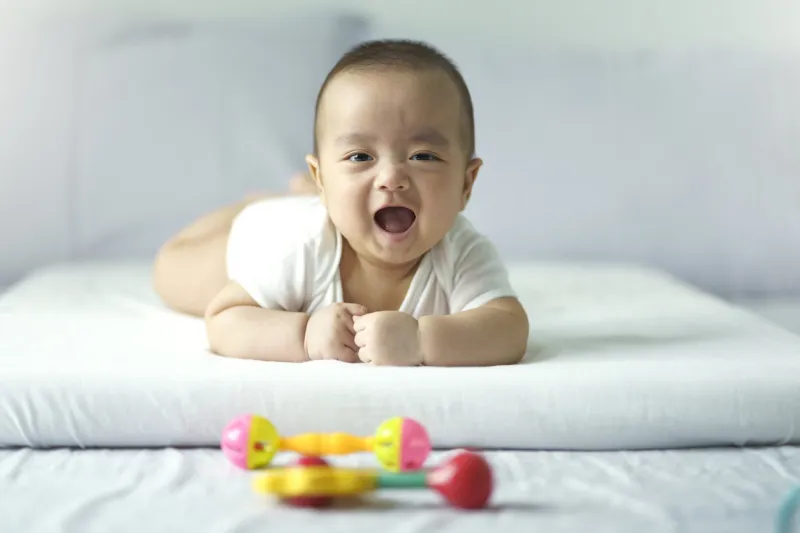 asian cute baby in white sunny bedroom newborn child relaxing on bed nursery for young children textile and bedding for kid family morning at home new born kid during tummy time with toy