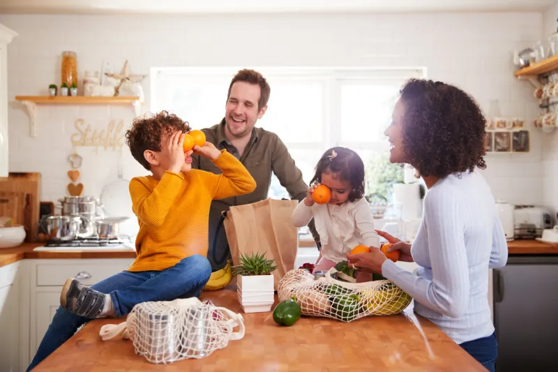family returning home from shopping trip using plastic free bags unpacking groceries in kitchen