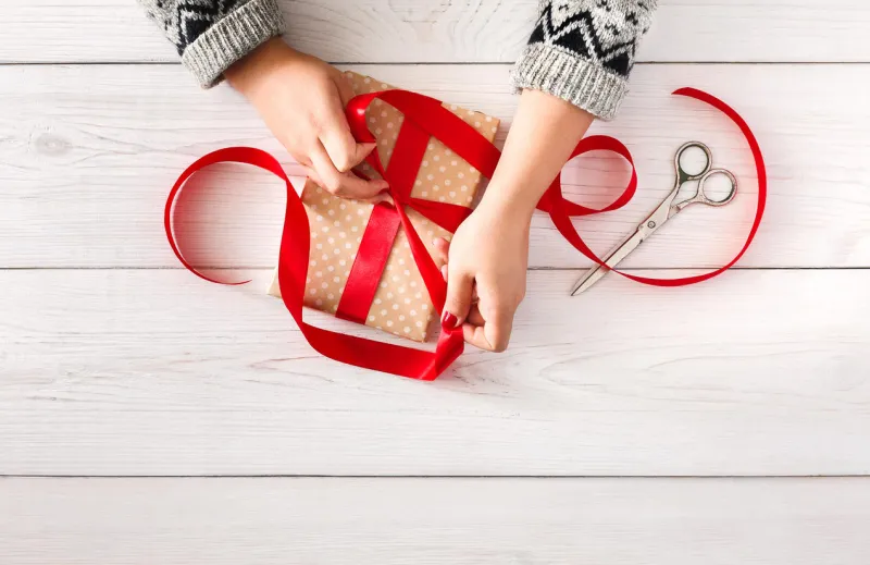 diy hobby mains de femme emballage de noël ou d'autres vacances fait main présent en papier avec ruban rouge faisant arc à la boîte actuelle, décoration de ciseaux cadeaux sur une table en bois blanc, vue de dessus