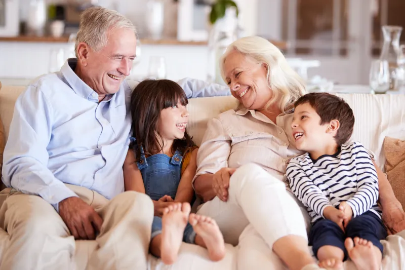 white senior couple and their grandchildren sitting on a sofa together smiling at each other