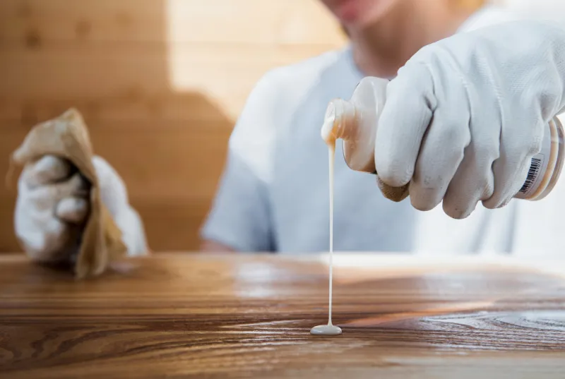 a girl in work gloves pours oil on a wooden tabletop coating wood with oil