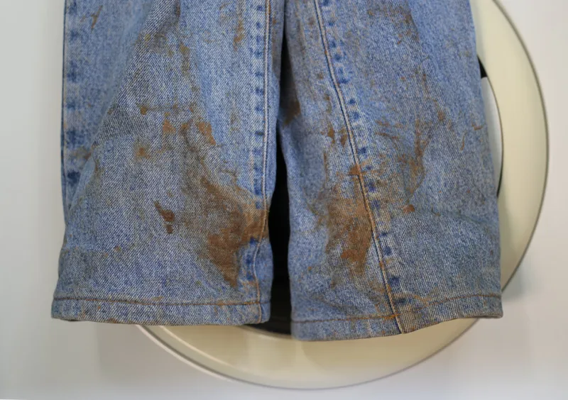 muddy jeans on a washing machine mud stain on jeans stained jeans before laundry the stain is metaphore for embarrassment, guilt, shame