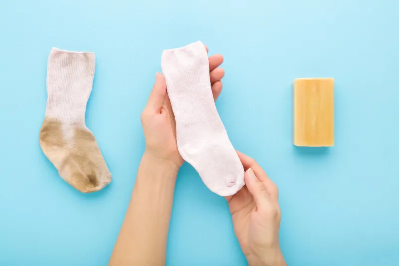 young adult woman hands showing clean child sock after washing with household soap on light blue table background pastel color compare dirty and clean socks closeup point of view shot top view