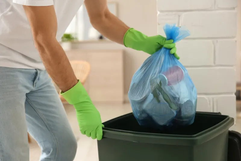 man throwing garbage bag into bin at home, closeup