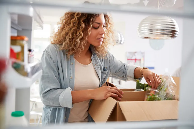 view looking out from inside of refrigerator as woman unpacks online home food delivery