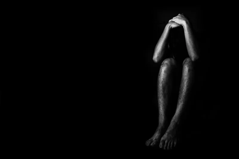 a man sitting on ground with arm around lower head, sexual violence , sexual abuse, human trafficking concept with shadow edge in white tone