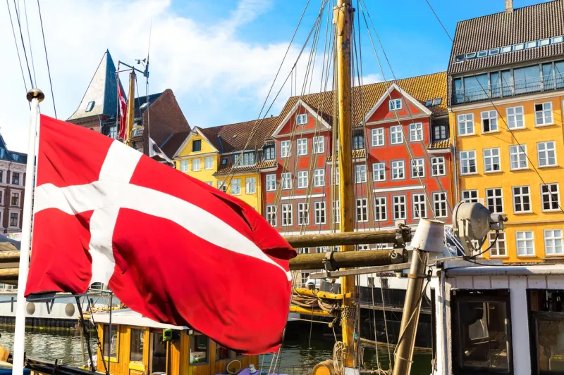 copenhagen iconic view famous old nyhavn port in the center of copenhagen, denmark during summer sunny day with denmark flag on the foreground